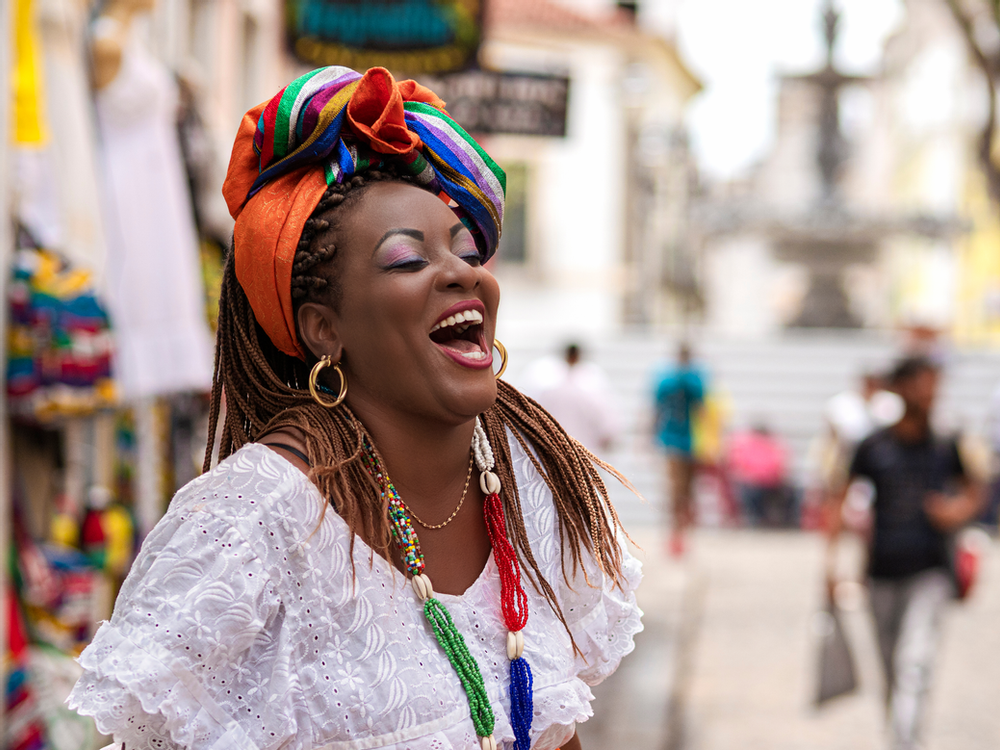 beautiful Black woman in a headwrap laughing on a busy street