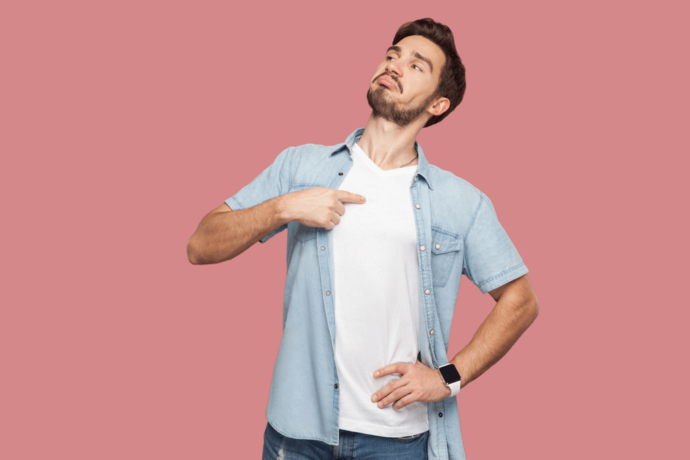smug looking young man pointing at himself against a plain pink background