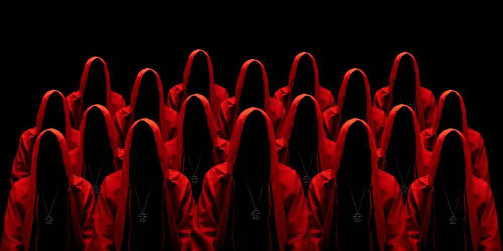 a group of red-hooded figures with their faces concealed, all wearing an amulet; black background