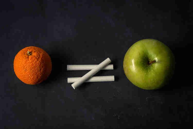 on a black chalkboard, an orange to the left with three chalks in the shape of a not-equal sign and a green apple on the right