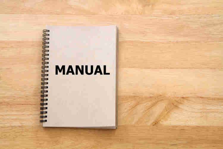 a notebook with "MANUAL" in bold on the front cover on a wooden table