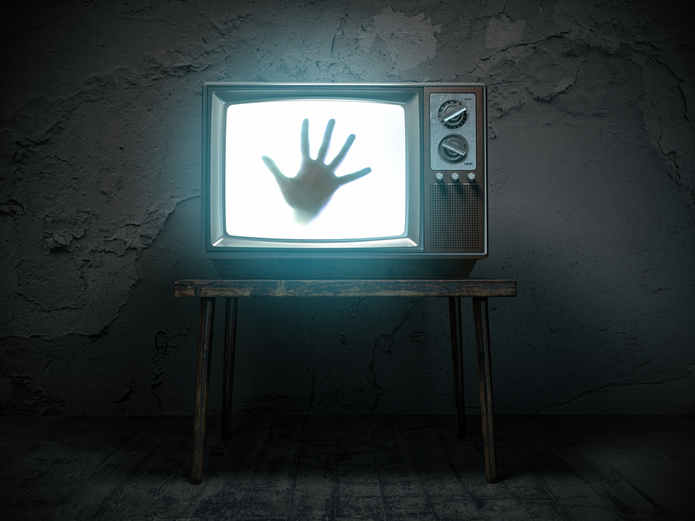 an image of an old fashioned television on a stool turned on, with a hand pressed against the glass