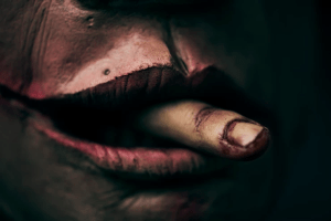 closeup image of an eerie mannequin-like figure with a severed finger in their mouth