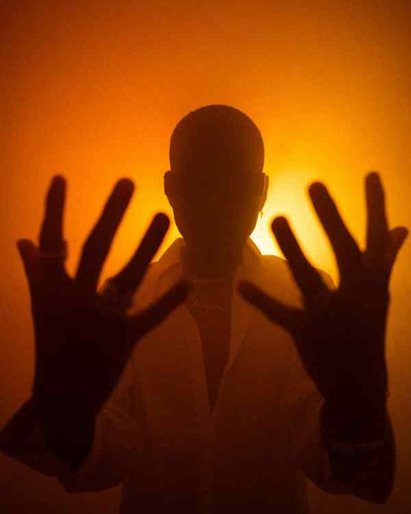 silhouette of a man in sunglasses against a yellow background holding up his hands