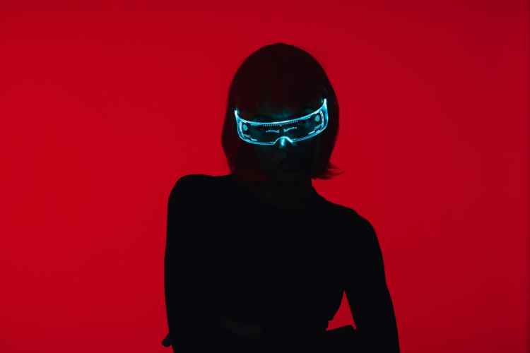 photo of a woman in black against a red background wearing cybernetic eyewear