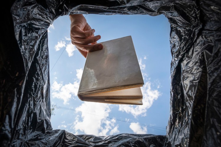 bottom-up view of a hand holding a book over a trash can