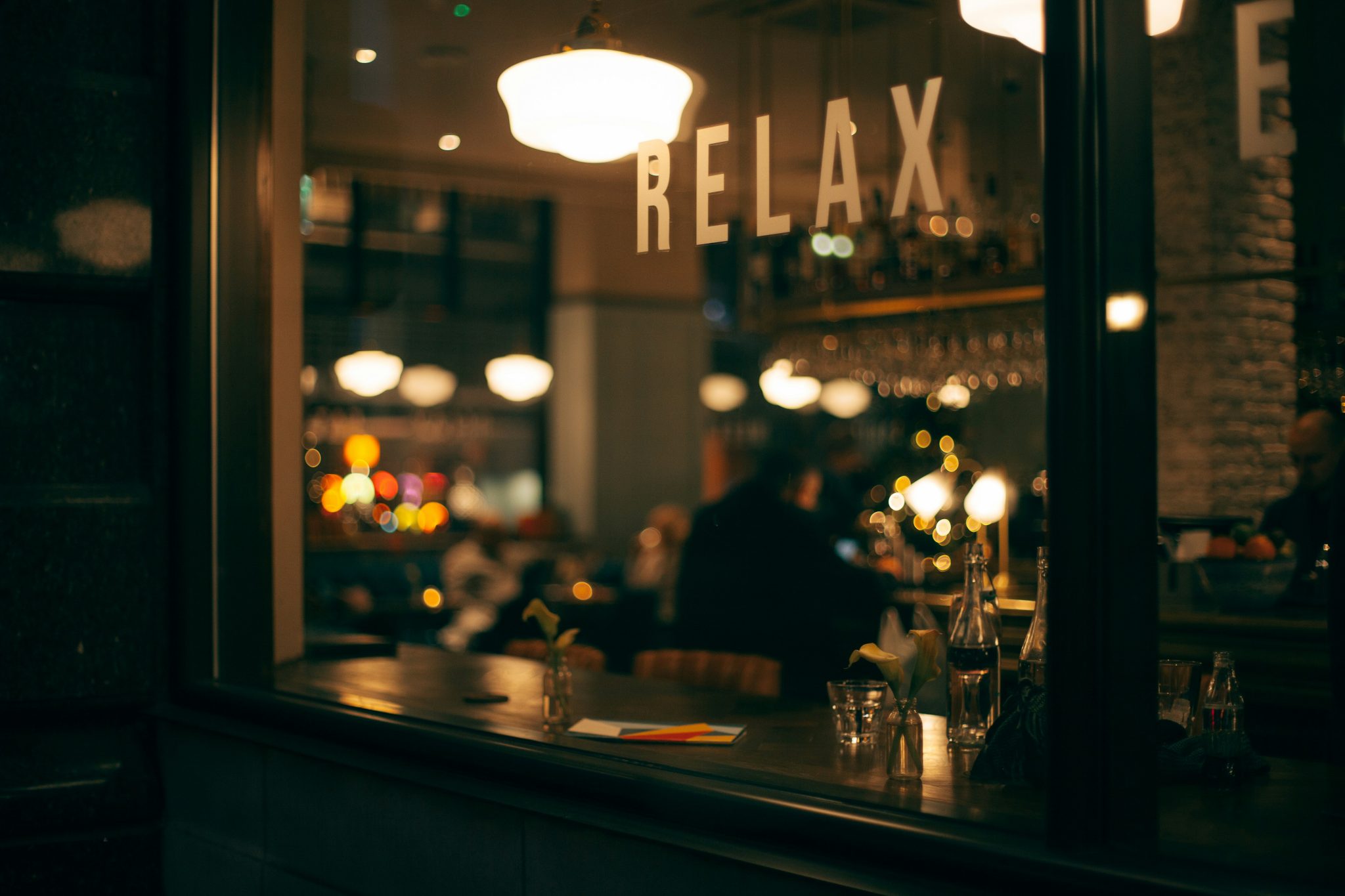 photo of a person sitting inside a cozy restaurant at night with a white sign above him reading, "Relax"