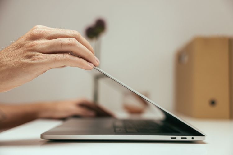 A close-up of a hand closing a laptop in a clean and minimal office setting, symbolizing stepping away when you have writing anxiety