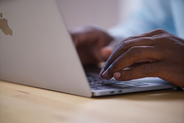 person typing on a laptop keyboard on a wooden surface