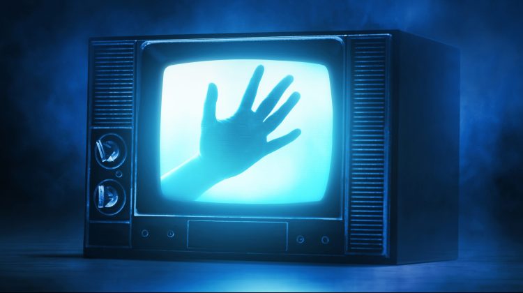 Image of a dark room with an analog TV. A hang is pressed against the screen