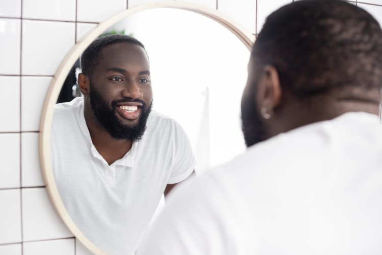 Black man in a white t-shirt smiling in the bathroom mirror