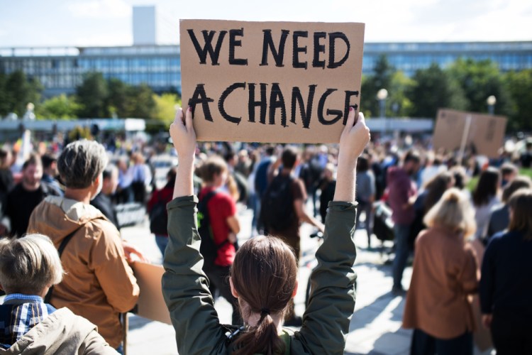 Rear view of a political protest and a cardboard sign being held up that says "We need a change."