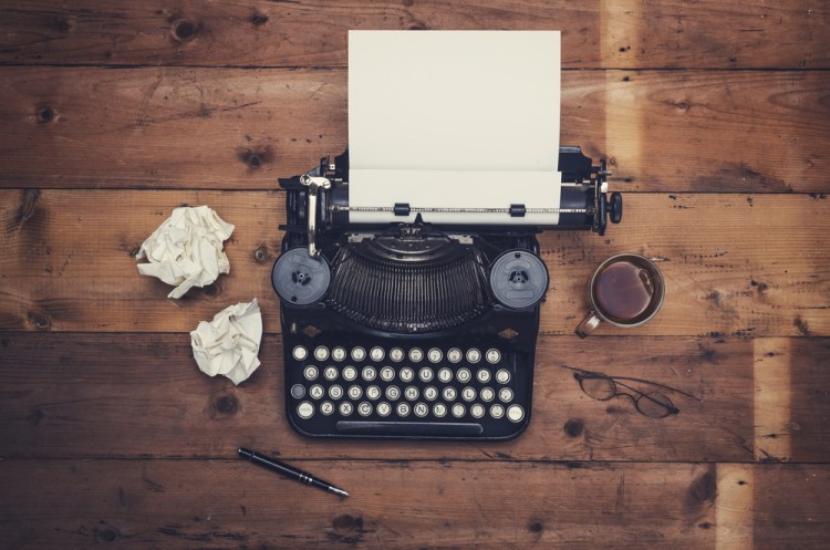 Top view of a typewriter on a wooden table with crumpled pieces of paper next to it. Writer's block concept