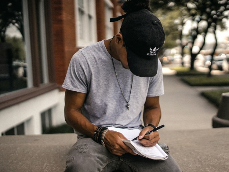 man sitting on a bench writing in a notebook