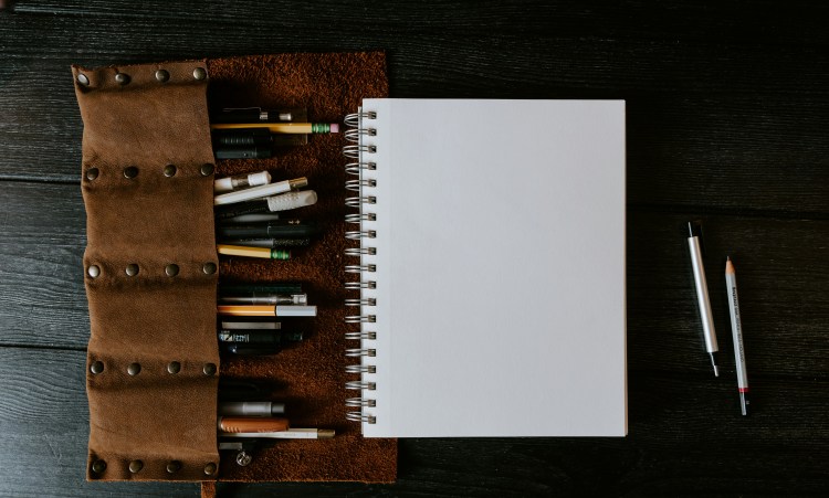 photo of a blank spiral notebook with a pouch full of pens and pencils next to it