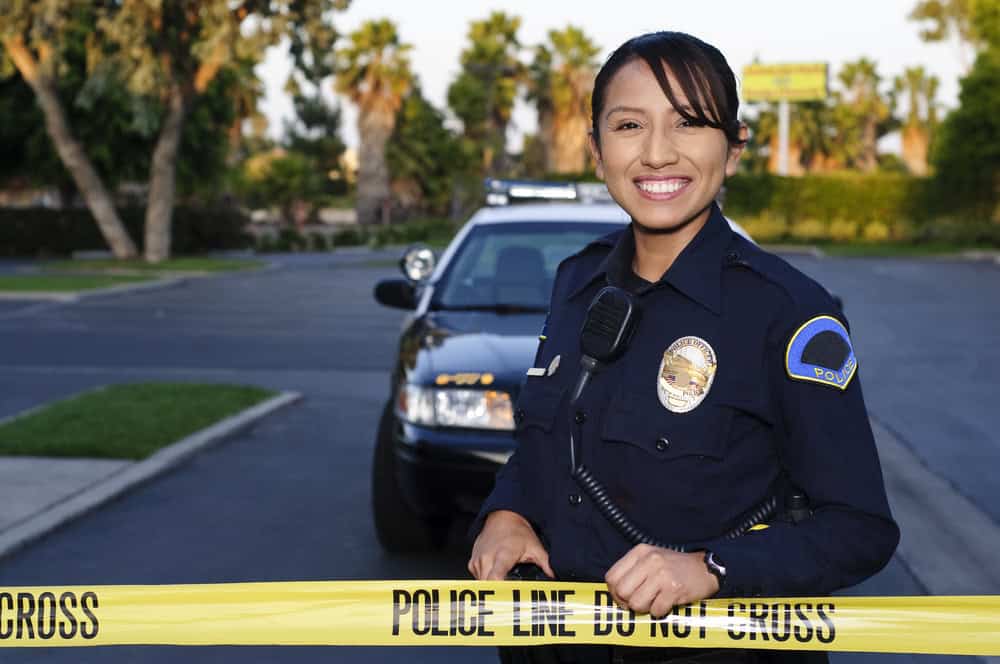A Hispanic female police officer holding crime scene tape; copaganda in media concept
